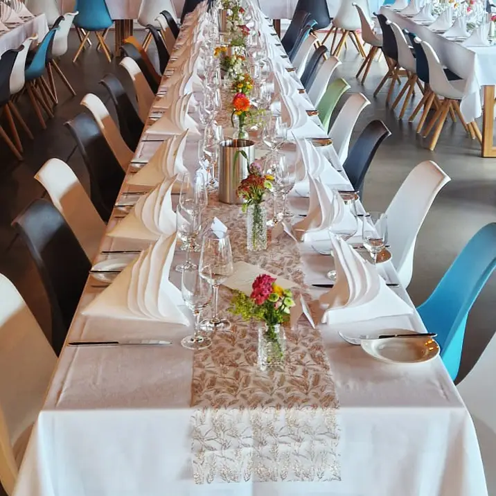 Ein langer Tisch, festlich und elegant gedeckt in WeiĂź, mit einer Tischdecke, weiĂźen Servietten und Rosen.