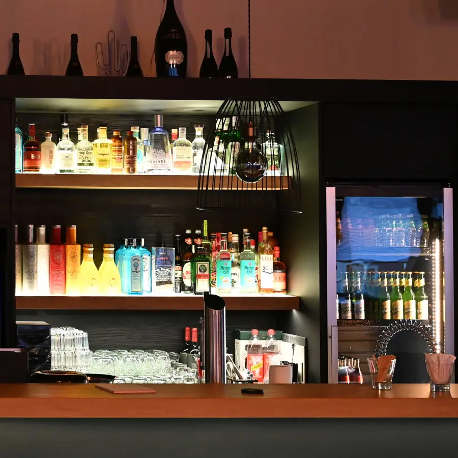 Eine kleine, elegante Bar, deren Flaschen und Gläser durch eine stimmungsvolle Beleuchtung auffallen.