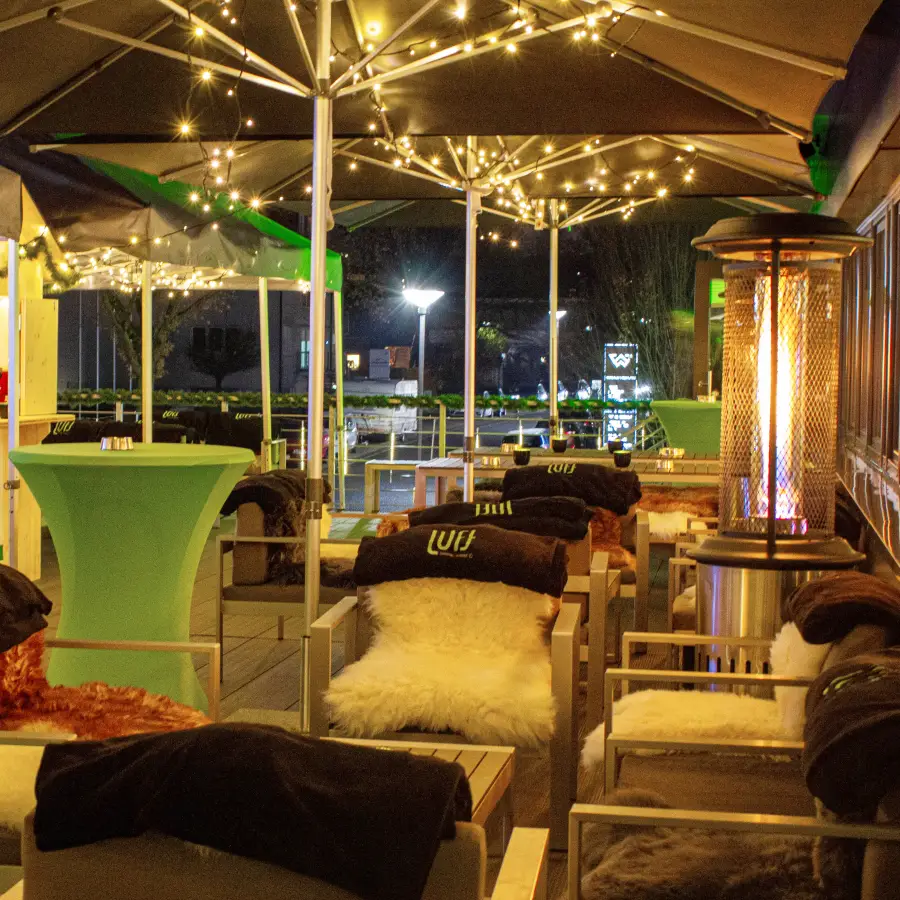 Eine Dachterrasse, die bei Nacht mit Sitzgelegenheiten, einer gemĂĽtlichen Lichterkette und Heizstrahlern ausgestattet ist.